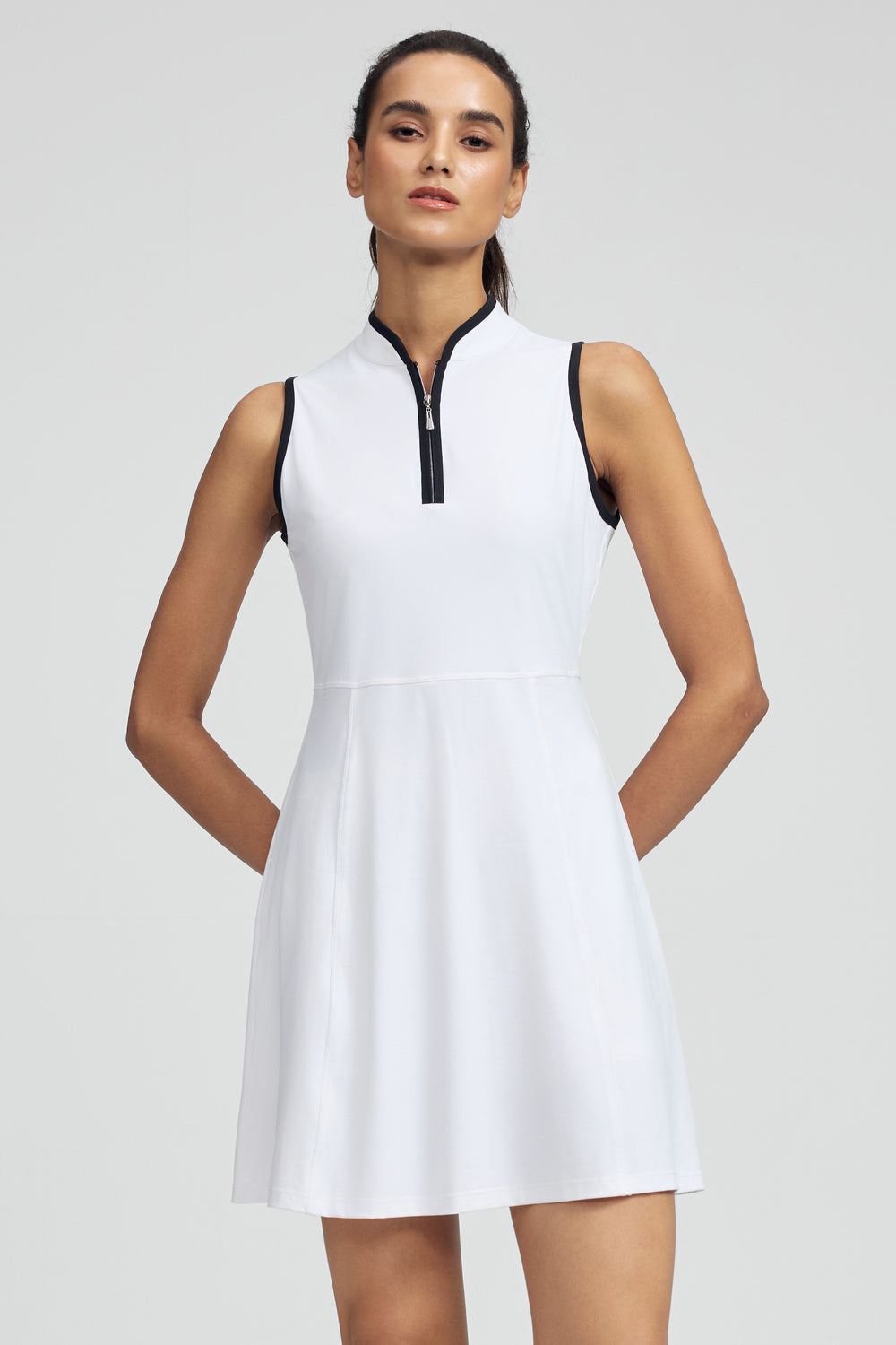 Woman wearing a white sleeveless golf dress with a black zipper on a light gray background