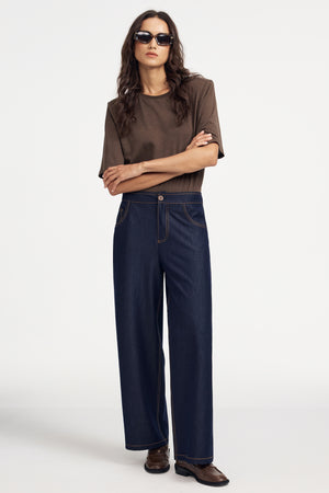 Woman wearing a premium brown linen bodysuit and blue jeans on a grey background