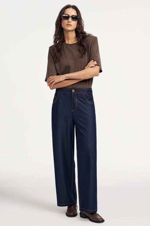 Woman wearing a premium brown linen bodysuit and blue jeans on a grey background